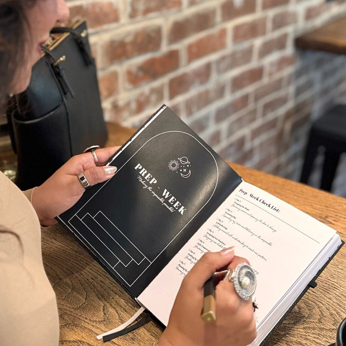 Person sitting at a table with a planner and pen, in a casual setting.